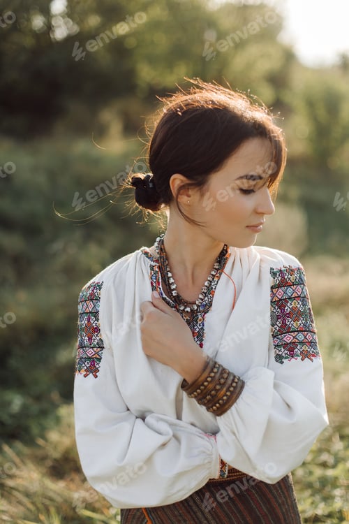 Preview: Young woman in traditional national embroidered shirt and skirt on nature at sunset.