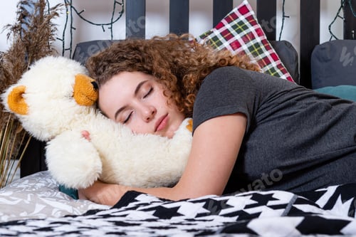 Preview: a young curly teenager woman with a teddy bear fell asleep in bed