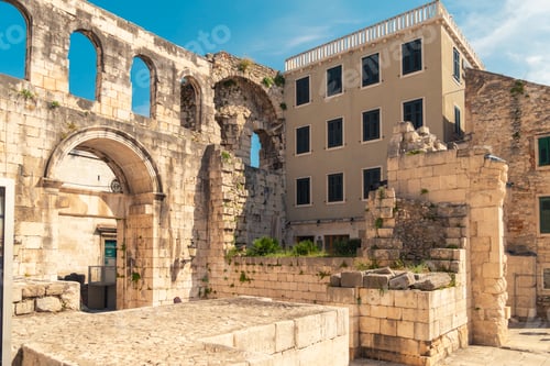 Preview: Ancient stone arches stand beside a modern building under a clear blue sky, blending