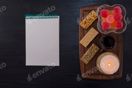 Preview: A glass of tea served with marmelades and sesame waffles on a wooden platter with a notebook aside