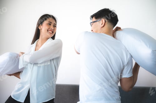 Preview: young Asian couple having pillow fight on bed in the morning, relaxing and happy at home