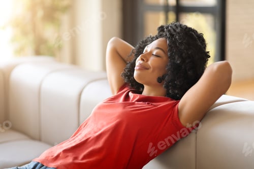 Preview: Home Comfort. Portrait Of Smiling Young Black Woman Leaning Back On Couch