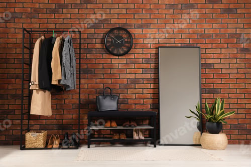 Preview: Stylish hallway with coat rack, mirror and shoe storage bench near brick wall. Interior design