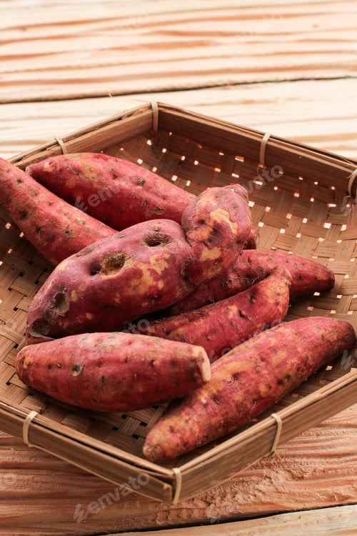 Preview: Red Sweet potato in a woven basket over rustic wooden background closeup