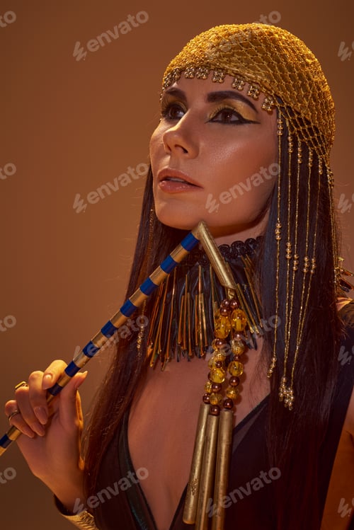 Preview: Portrait of woman in stylish egyptian look holding flair while posing isolated on brown