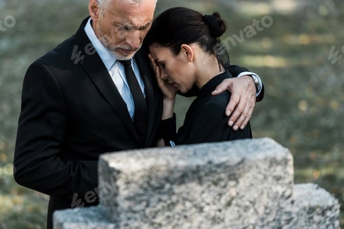 Preview: selective focus of senior man hugging upset woman near tombstone
