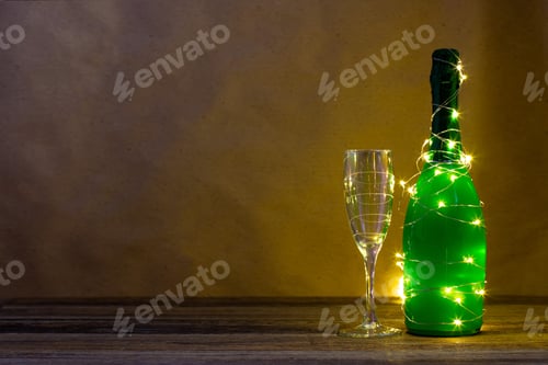 Visualização: uma garrafa de champanhe verde embrulhada em uma guirlanda brilhante como uma árvore de Natal e um copo. Ano novo