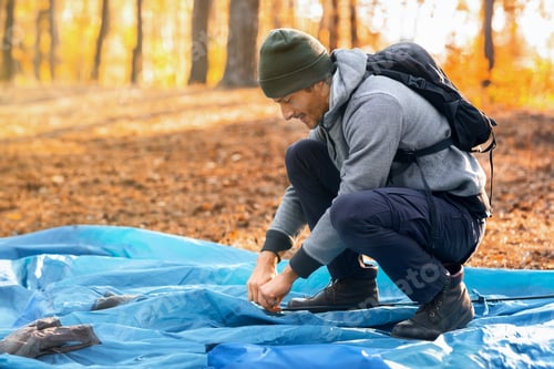 Preview: Young man backpacker setting tent, camping at golden forest