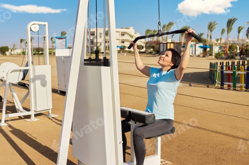 Preview: Mature woman doing sports exercises on outdoor simulators
