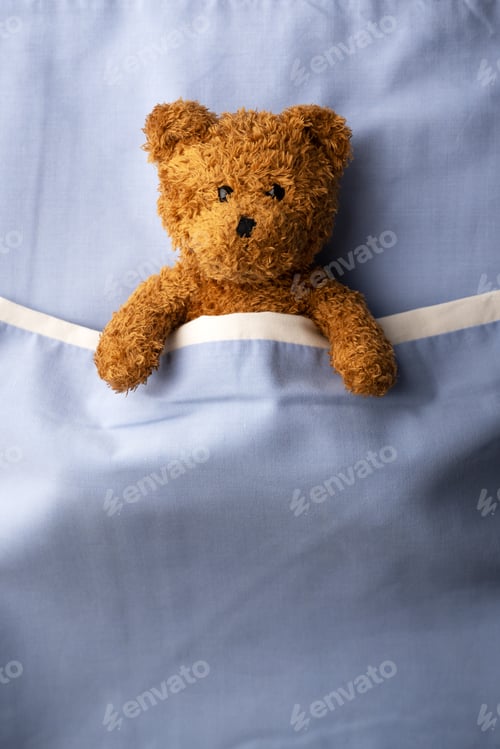 Preview: Brown teddy bear laying on blue bed