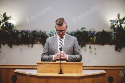 Preview: Male in a grey suit preaching words of the Holy Bible at the altar of a church