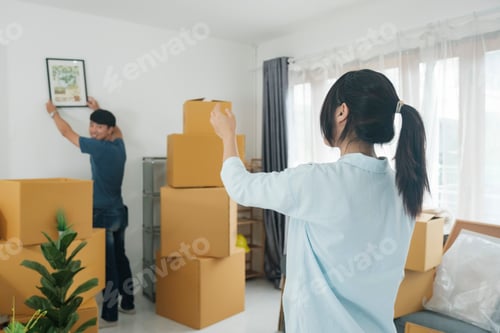 Preview: Man hanging picture on white wall in room. Interior design