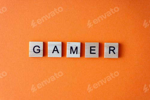 Preview: Gamer word. The phrase is laid out in wooden letters top view. Orange flat lay background.