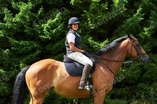 Preview: Side view of mature woman on horseback wearing riding hat and boots looking at camera smiling