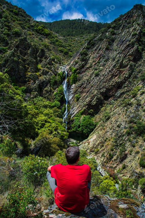 Preview: Man relaxing contemplating waterfall in a mountain landscape