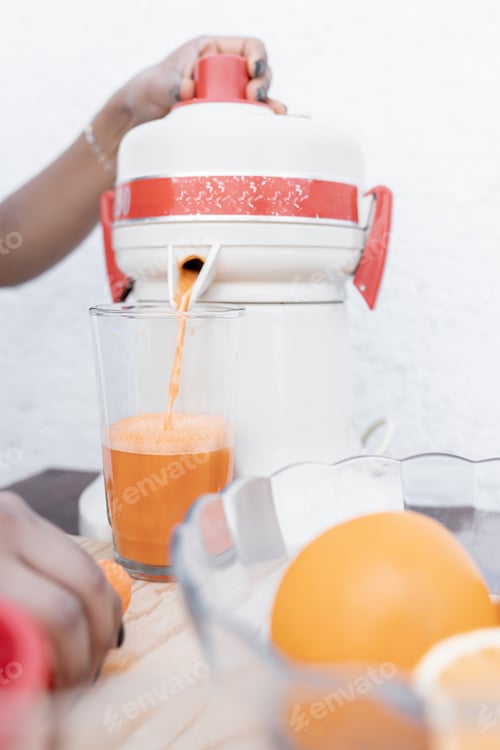 Preview: A young Hispanic woman is using a traditional squeezer to make carrot and orange juice