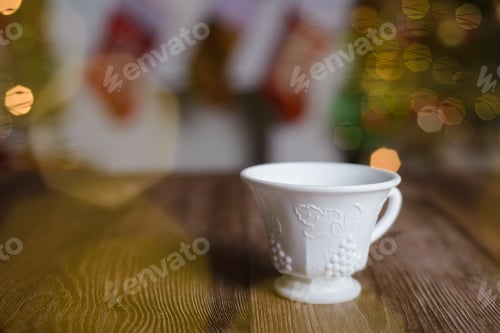 Preview: White tea cup with embossed engraving on wooden table with Christmas background.