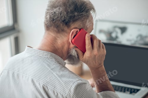 Preview: A man in white tshirt with a smartphone in hands working at home