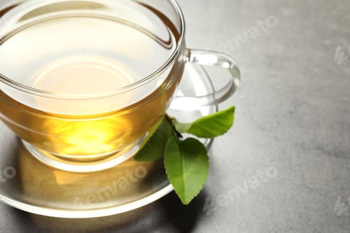 Preview: Cup of green tea and leaves on grey table, closeup. Space for text