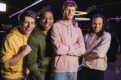 Preview: Cheerful interracial friends looking at camera in gaming club