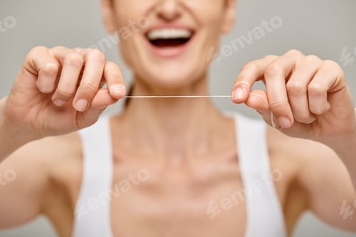 Preview: focus on dental floss on grey background, cropped view of happy woman promoting oral hygiene