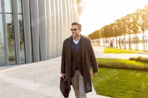 Preview: Businessman strolling confidently beside modern architecture during sunset glow