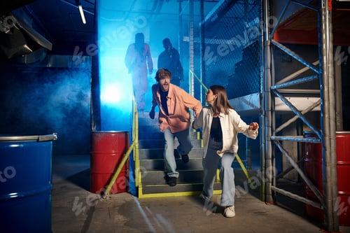 Preview: young man and woman running from scary people in gas masks and orange ppe suits in escape room