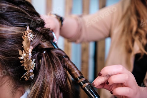 Preview: Hairstylist curling a client hair while doing her wedding hairstyle at the hairdressing salon.