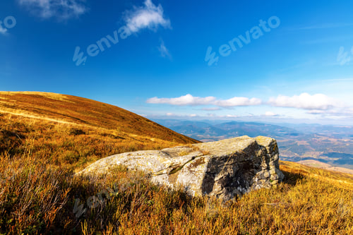 Preview: Big old stone lies on grassy hill in highland under blue sky
