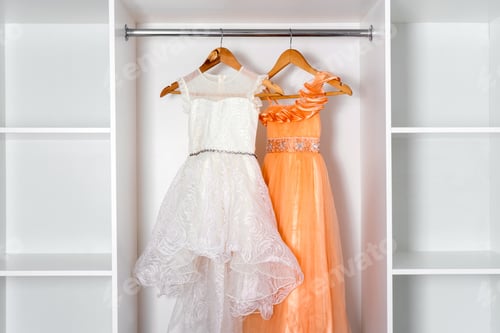 Preview: White and orange puffy dresses hang on hangers in modern white dressing room.