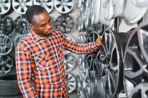 Preview: African american Car mechanic holding car rims ready to mount the wheels in workshop