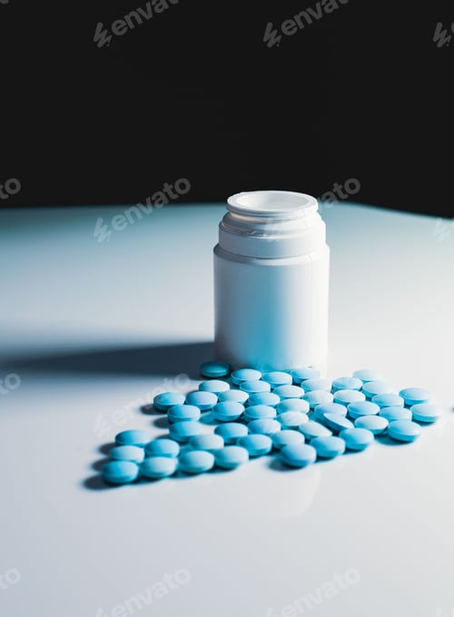Preview: Vertical shot of several blue pills spilled by a plastic bottle on a white background
