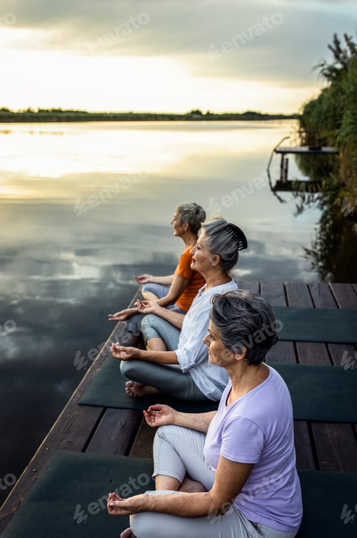Preview: Group of senior woman doing yoga exercises by the lake.