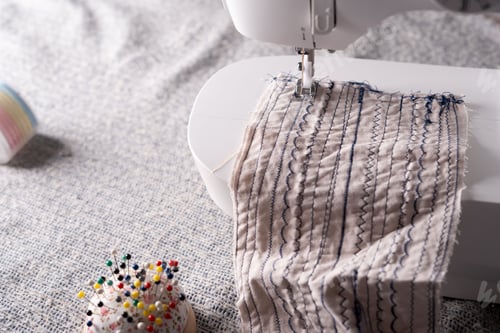Preview: Sewing machine stitching patterned fabric, vibrant pins, threads: tailor's textured surface tool.