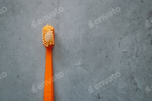 Preview: Orange plastic toothbrush with toothpaste on gray concrete table. Dental clinic banner design