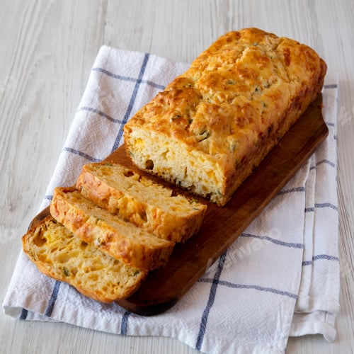 Preview: Homemade Cheesy Bread Loaf on a rustic wooden board on a white wooden background, side view.