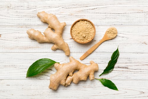 Preview: Finely dry Ginger powder in bowl with green leaves isolated on colored background. top view flat lay