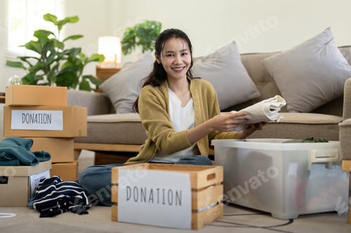 Preview: Woman asian holding donation box full with clothes and select clothes. Concept of donation and