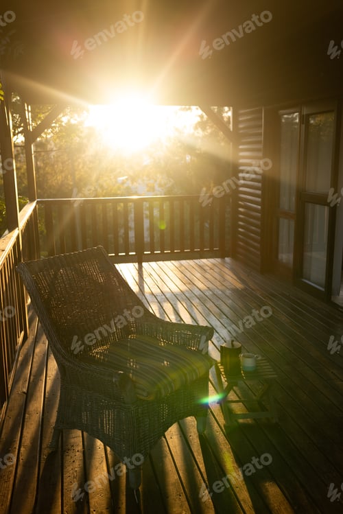 Preview: Vertical image of balcony of log cabin with armchair and mug of coffee on sunny day