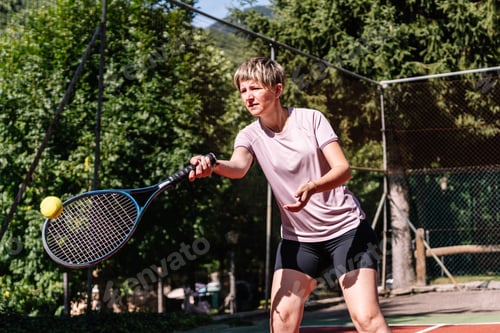 Preview: Female tennis player hitting ball with racket on outdoor court