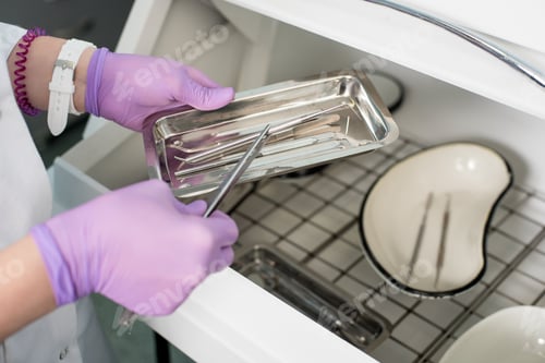 Preview: Doctor's assistant with gloved hands is picking dental tools from sterile storage in dental office