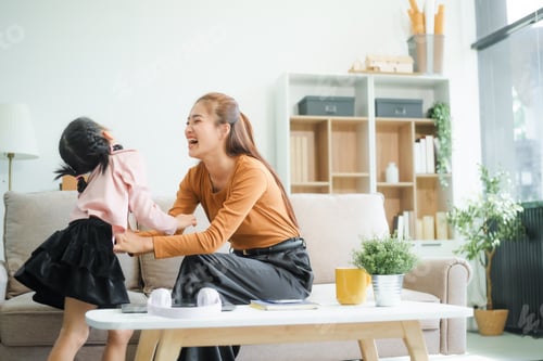 Preview: An Asian mother and her adorable daughter sit on the sofa in their living room, enjoying online
