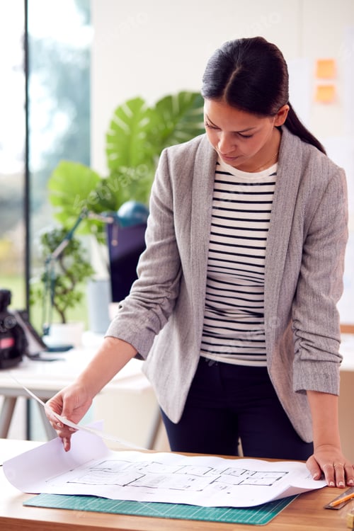 Preview: Female Architect Standing Working In Office Studying Plans For New Building