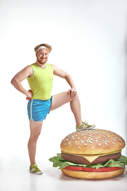Preview: Red haired, bearded, plump man put his leg to a huge sandwich