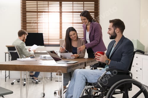 Preview: Young man in wheelchair with colleagues at workplace