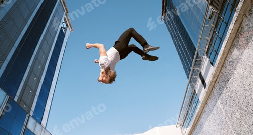 Preview: caucasian blond boy doing a backflip and parkour with blue sky in the background