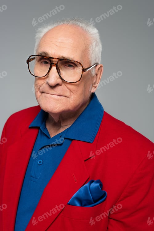 Preview: portrait of serious elderly man in red blazer and glasses isolated on grey