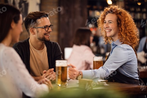 Preview: Cheerful waitress serving beer to her guests in a bar.