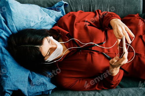 Preview: woman with phone and mask on her couch during corona virus outbreak