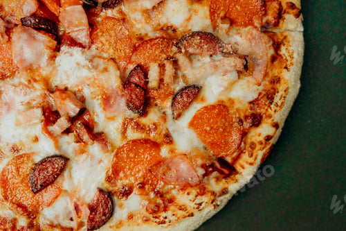Preview: Pizza topped with pepperoni and ham on a green surface ready to enjoy